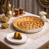 Dessert platter with baklava, tea, and nuts on a decorative table setting.